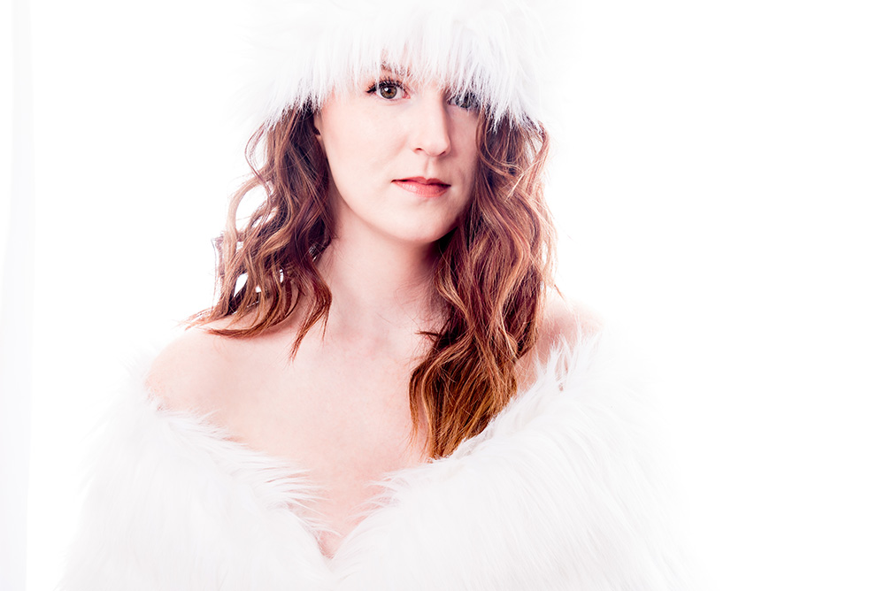 Red haired, brown eyed girl wearing white fur hat and top on white background in high key photograph. Alyssa Bryn Photography. Bryssa. Bryssa Blog.