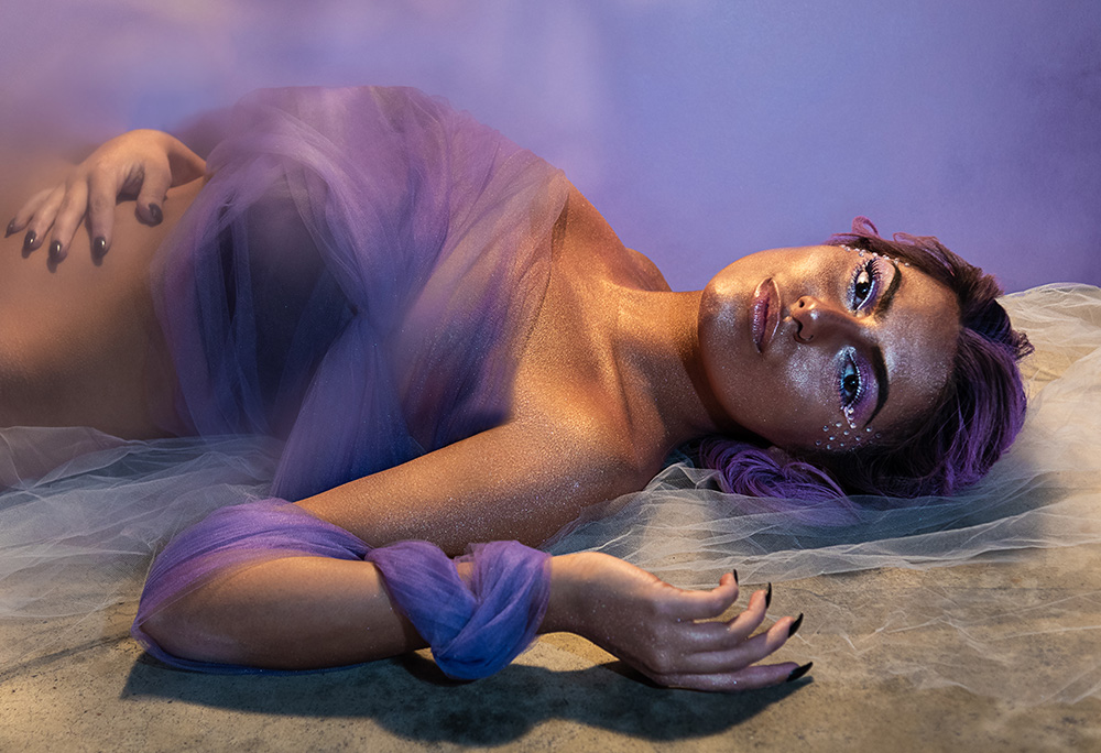Girl laying on floor wearing sheer purple fabric with heavy gold body glitter, purple eye makeup, purple hair and rhinestones. Alyssa Bryn Photography. Bryssa. Bryssa Blog.