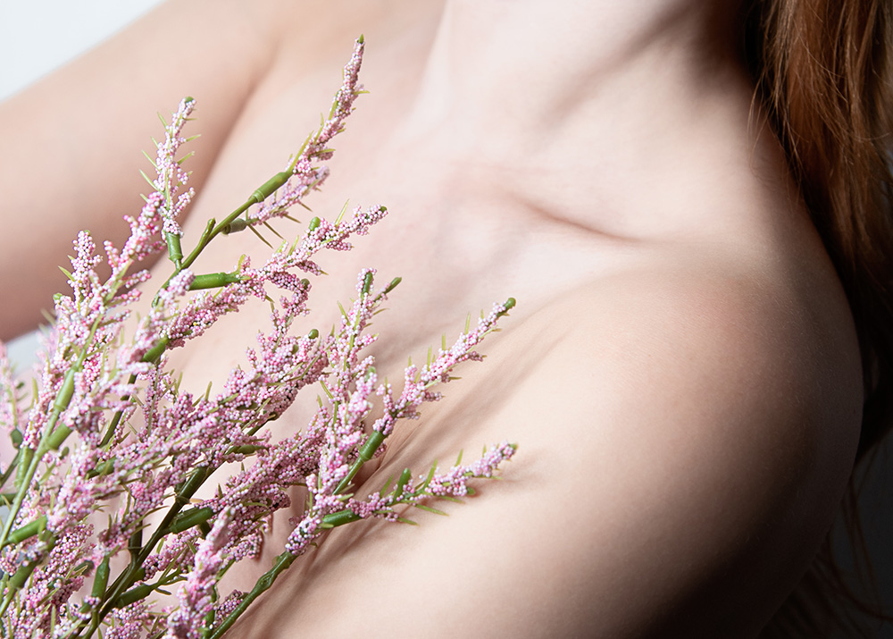 Girl holding up little pink flowers to her chest near her coller bone. Alyssa Bryn Photography. Bryssa. Bryssa Blog.
