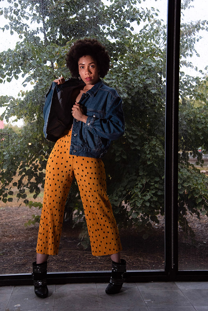 African American girl with beautiful afro stands against a window jean jacket and yellow pants. Alyssa Bryn Photography. Bryssa. Bryssa Blog.