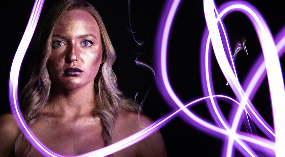 Blonde hair blue eye girl covered in gold body glitter sits still white purple neon light is painted around her. Alyssa Bryn Photography. Bryssa. Bryssa Blog.