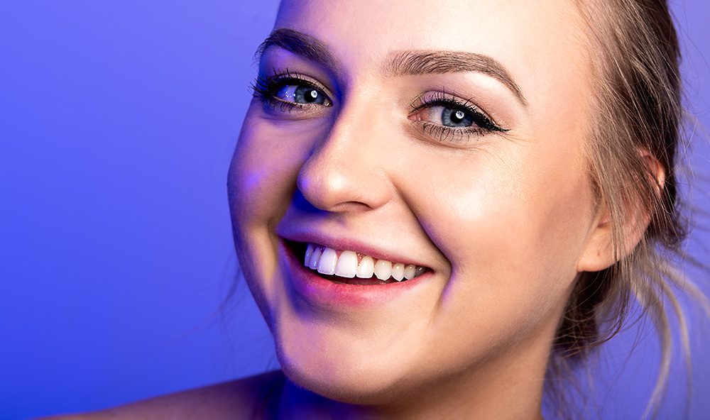 Blonde hair blue eye girl smiles with a perfect white smile on a bright blue background. Alyssa Bryn Photography. Bryssa. Bryssa Blog.