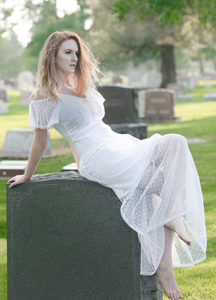 Red hair girl in a white dress leans back on headstone in lush green cemetary. Alyssa Bryn Photography. Bryssa. Bryssa Blog.