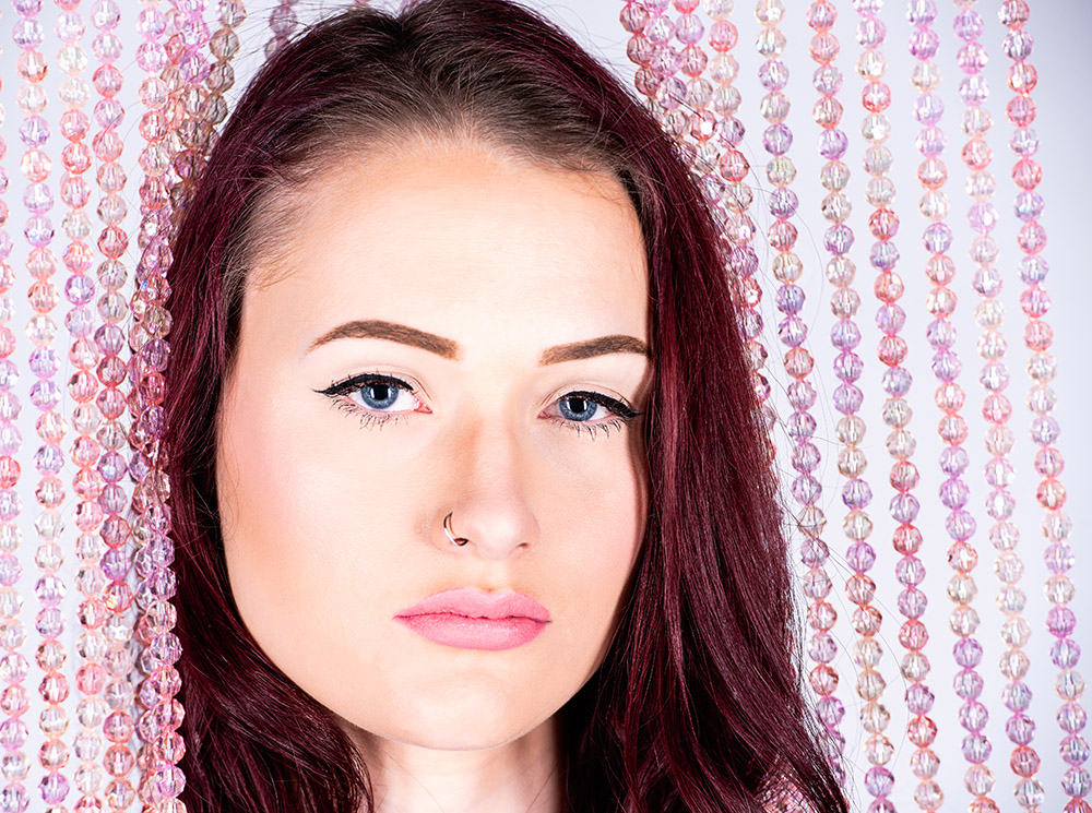 Dark hair blue eyed girl wearing pink lipstick and silver nose ring posing with strands of pink glass beads. Alyssa Bryn Photography. Bryssa. Bryssa Blog.