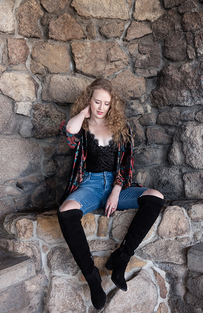 Blonde curly haired girl sits on natural rock bench wearing knee high black boots, ripped skinny jeans, black lace bodysuite, and red flower patterned jacket. Alyssa Bryn Photography. Bryssa. Bryssa Blog.