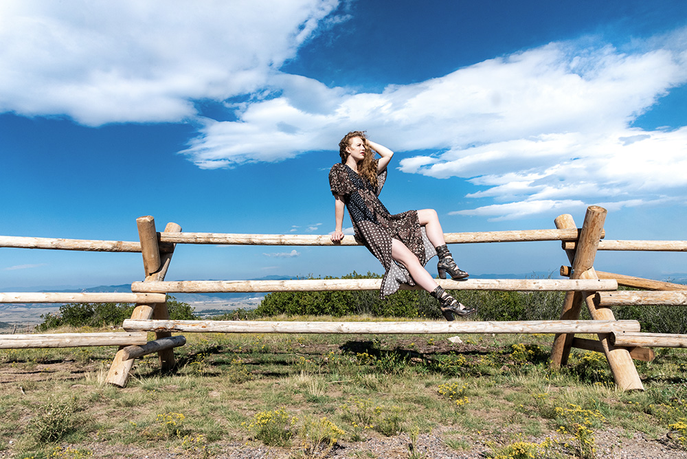 Girl in natural park sits on wooden fence wearing flower patterned dress and high heels. Alyssa Bryn Photography. Bryssa. Bryssa Blog.