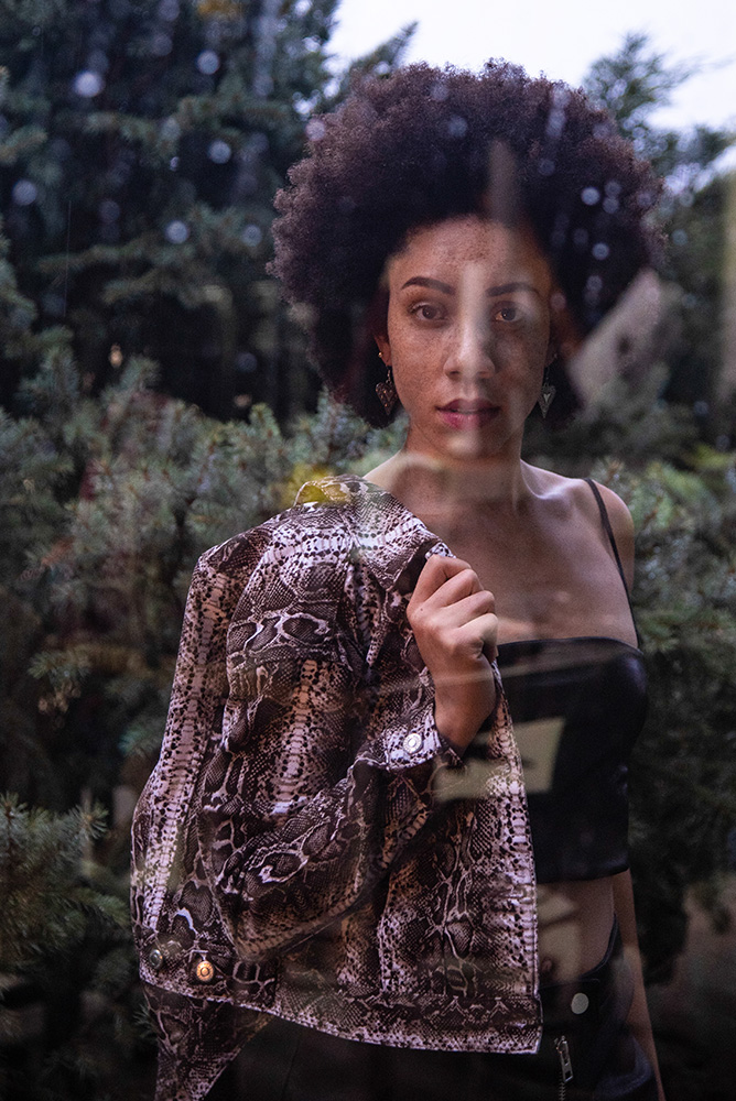 African American girl with beautiful afro stands through the window in the rain wearing a black leather crop top and snake print jacket. Alyssa Bryn Photography. Bryssa. Bryssa Blog.